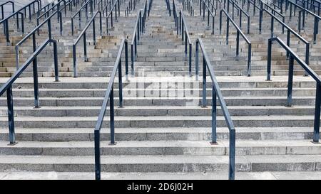 Externe mehrstufige Steintreppe. Es gibt viele Treppen und Geländer aus Metall. Viele Schritte in einer städtischen Umgebung, symbolisch abstrakt zurück Stockfoto