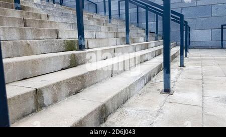 Externe mehrstufige Steintreppe. Es gibt viele Treppen und Geländer aus Metall. Viele Schritte in einer städtischen Umgebung, symbolisch abstrakt zurück Stockfoto