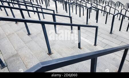 Externe mehrstufige Steintreppe. Es gibt viele Treppen und Geländer aus Metall. Viele Schritte in einer städtischen Umgebung, symbolisch abstrakt zurück Stockfoto