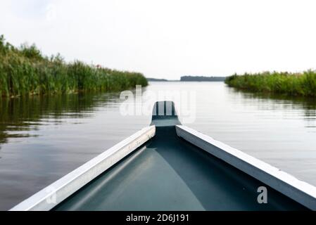 Foto aus einem Holzboot, das Bug des Bootes sichtbar, im Hintergrund ein verschwommener See und Schilf. Stockfoto