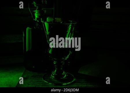 Blick auf isoliertes Absinth-Glas und Flasche in düsterem Grün Nachtatmosphäre Stockfoto