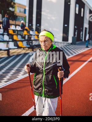 Alte Frau in Sportbekleidung übt nordic Walking im Freien auf Gummi-Laufband im Stadion. Ältere Frauen gehen auf dem skandinavischen Weg mit Trekkingstöcken Stockfoto