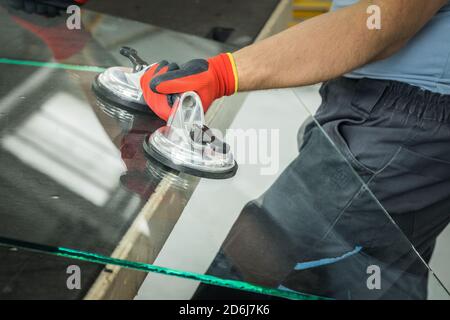 Der Glasier verwendet einen Sauger für Fenster. Glaswerkstatt, hebt der Mann die Scheibe aus dickem Glas auf den Tisch mit Hilfe von spezialisierten Werkzeugen Stockfoto