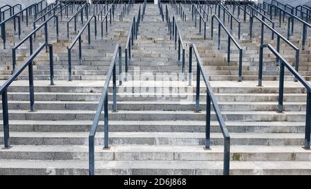 Externe mehrstufige Steintreppe. Es gibt viele Treppen und Geländer aus Metall. Viele Schritte in einer städtischen Umgebung, symbolisch abstrakt zurück Stockfoto