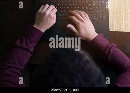 Junge schwarze männliche Entwickler sitzen in Pizza-Restaurant, trinken Kaffee oder Tee und arbeiten mit Laptop. Stockfoto