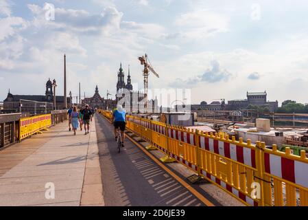 Die Renovierung einer alten, historischen Augustusbrücke über die Elbe. Menschen, die auf einem vorübergehenden Seitenweg gehen, der von einem gelben Zaun begrenzt ist. Dresden, Deutschland Stockfoto