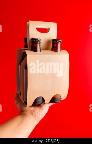 Hand hält eine vierpackige Bierpräsentation mit rotem Hintergrund Stockfoto