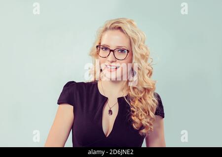 Lächelnde Frau in einer Brille, die Sie mit einem Lächeln ansieht. Kaukasische Geschäftsperson in schwarzem formellen Kleid, lange blonde lockiges Haar isol Stockfoto