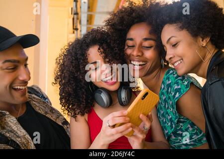 Portrait von Afro-Freunden, die Spaß in der Stadt haben und viel Zeit miteinander verbringen, während sie ihr Handy benutzen. Freundschaft und Lifestyle-Konzept. Stockfoto