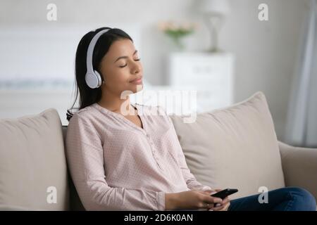 Junge Birazialfrau in Kopfhörern hören Musik auf Zelle Stockfoto