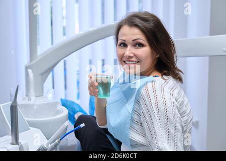 Glückliche Mitte Erwachsene Frau Patient in Zahnarztstuhl mit Glas Von Wasser Stockfoto