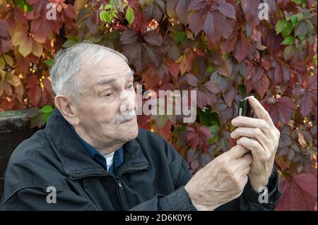 Ältere aktive gutaussehende Mann mit einem Schnurrbart nimmt ein Selfie mit einem Handy. Ein älterer Mann sieht die Kamera sprechend und lächelnd an Stockfoto