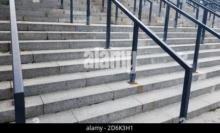 Externe mehrstufige Steintreppe. Es gibt viele Treppen und Geländer aus Metall. Viele Schritte in einer städtischen Umgebung, symbolisch abstrakt zurück Stockfoto