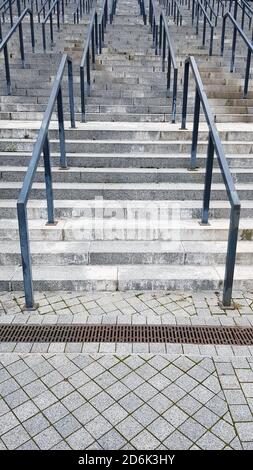 Externe mehrstufige Steintreppe. Es gibt viele Treppen und Geländer aus Metall. Viele Schritte in einer städtischen Umgebung, symbolisch abstrakt zurück Stockfoto