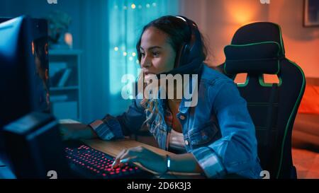 Aufgeregt und konzentriert Gamer Girl in Headset mit Mikrofon spielen Online-Video-Spiel auf ihrem Personal Computer. Sie spricht mit anderen Spielern. Zimmer und PC haben Stockfoto