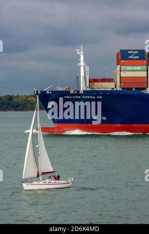 yacht, die in der Nähe des Bogens eines großen Containerschiffes im Dornkanal auf dem Anflug zum Hafen von southampton segelt, dockt in der solent-Schifffahrt an. Stockfoto