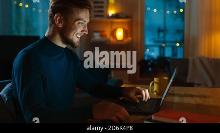 Abend zu Hause: Portrait von Handsome man sitzt an seinem Schreibtisch arbeiten auf einem Laptop. Lächelnder Freiberufler beim Arbeiten am Computer. Seitenansicht. Stockfoto