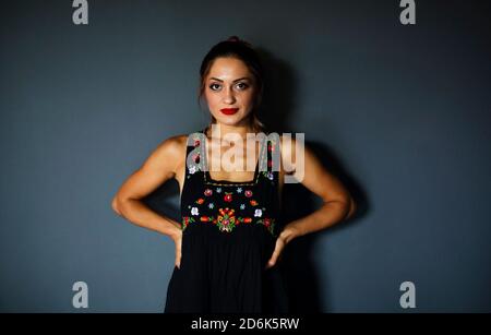 Junge ethnische Dame in stilvollem schwarzen Kleid mit traditionellen mexikanischen Farbenfrohe Blumenstickerei an der dunklen Wand Stockfoto