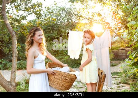 Charming kleines Mädchen helfen Mutter mit Weidenkorb während der Arbeit Chore und hängende Wäsche im Hinterhof im Sommer Abend Stockfoto