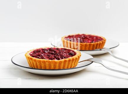 Leckere hausgemachte Kirschkäse-Tartlets auf weißem Holztisch. Vorderansicht vor weißem Hintergrund. Copyspace. Stockfoto