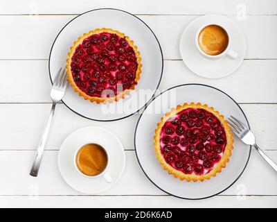 Zwei leckere hausgemachte Kirschkäse-Tartlets und zwei weiße Tassen Kaffee Espresso auf weißem Holztisch. Draufsicht. Stockfoto