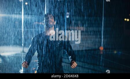 Starker muskulöser Fit junger Mann in dunkler Athletic Kleidung feiert seine sportlichen Leistungen. Er jubelt nachts in Heavy Rain mit einem Stockfoto