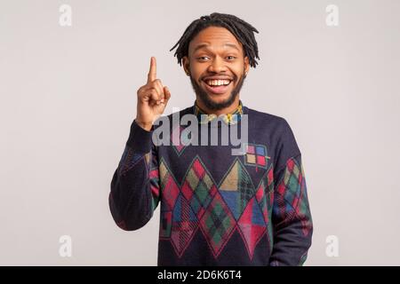 Extrem glücklich afrikanischen Kerl mit Dreadlocks im stilvollen Sweatshirt zeigt Finger nach oben mit toothy Lächeln auf Gesicht, clever smart Mann hat Idee, starten. ICH Stockfoto