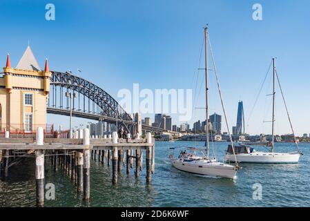 Mit der Sydney Harbour Bridge im Hintergrund wird eine schlanke Yacht in Lavender Bay vorbei am Luna Park, Milsons Point, Australien, hineingefahren Stockfoto