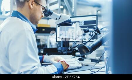 Arbeiter in der Elektronikfabrik in White Work Coat löten eine Leiterplatte über ein digitales Mikroskop. High-Tech-Fabrik. Stockfoto