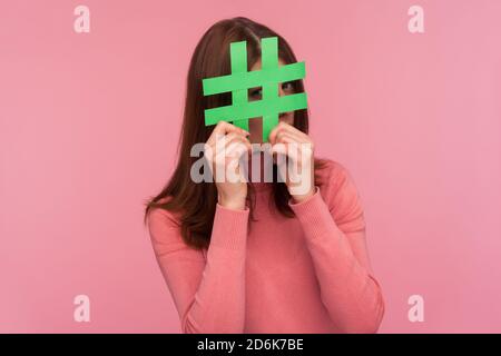 Neugierige Brünette Frau in rosa Pullover Blick durch grüne Hashtag Zeichen, auf der Suche nach richtigen Beiträge in den sozialen Medien, Spionage. Innenaufnahmen im Studio Stockfoto