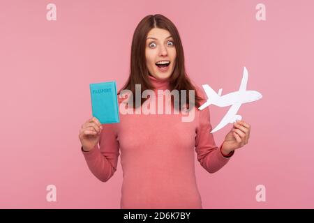 Schockiert Frau mit braunen Haaren in rosa Pullover in den Händen Papier Flugzeug und Pass halten, Vorbereitung für plötzliche Reise, erstaunt über Abenteuer. Innen s Stockfoto