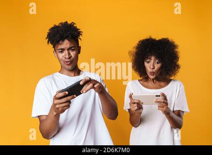 Foto von aufgeregt afroamerikanischen Menschen spielen Online-Spiel auf Mobiltelefone auf gelbem Hintergrund isoliert Stockfoto