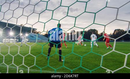 Aufgenommen von hinter dem Netz mit dem ganzen Stadion sichtbar. Fußball-Meisterschaft: Spieler Kick the Ball und Torwart ist bereit, Ziele zu verteidigen und fangen die Stockfoto