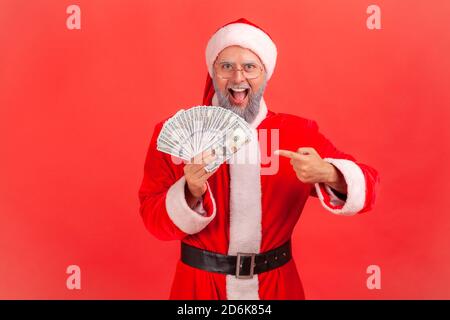 Extrem glücklich aufgeregt Mann im weihnachtsmann Kostüm Zeigefinger Bei Dollar-Banknoten hält er in der Hand und schaut in die Kamera Mit großen Augen und offenem mou Stockfoto