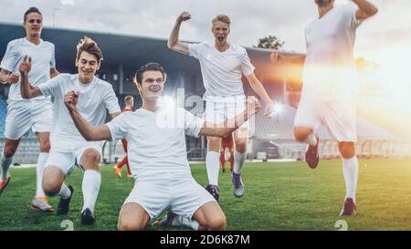 Kapitän der Fußball-Team steht auf den Knien feiert Awesome Victory, macht YES Gesture Champion Team schließt sich ihm. Erfolgreicher Happy Football Stockfoto