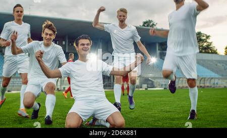 Kapitän der Fußball-Team steht auf den Knien feiert Awesome Victory, macht YES Gesture Champion Team schließt sich ihm. Erfolgreicher Happy Football Stockfoto