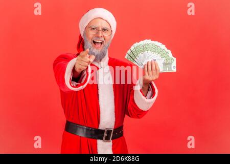 Extrem glücklich aufgeregt weihnachtsmann hält Spaß an Euro und zeigt den Finger auf Sie Blick auf Kamera, Urlaub Sieg. Innenaufnahme des Studios isoliert o Stockfoto