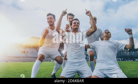 Kapitän der Fußball-Team steht auf den Knien feiert Awesome Victory, macht YES Gesture Champion Team schließt sich ihm. Erfolgreicher Happy Football Stockfoto