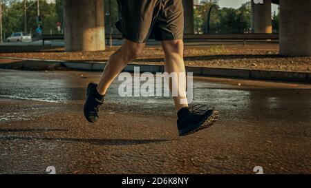 Nahaufnahme der muskulösen Athletic man Legs Running in the Street. Städtische Umwelt unter einer Brücke mit Autos im Hintergrund. Stockfoto