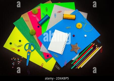Craft Concept - buntes Papppapier und Bleistifte, Leim, Schere, Fadenspulen, Clips und Perlen. Schreibwaren für Kinder. Stockfoto