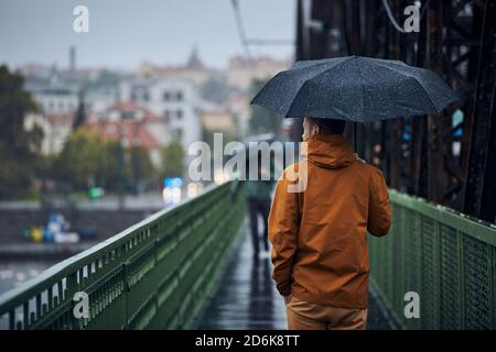 Junger Mann mit Regenschirm läuft bei starkem Regen auf der Brücke. Düsterer Tag in Prag, Tschechische Republik Stockfoto