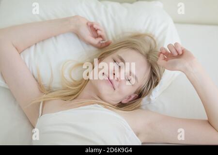 Schöne junge Frau im Bett aufwachen, während sie ihre Arme am Morgen entspannt aus einem guten Schlaf. Stockfoto