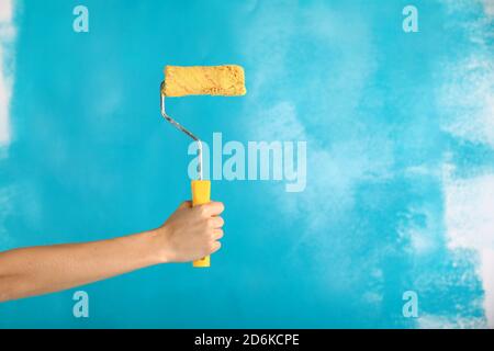 Nahaufnahme der weiblichen Hand halten Farbe gelb Rolle über blauen Hintergrund-Reparatur-, Bau-und Bauwerkzeuge Konzept. Praktisch und vielseitig Stockfoto