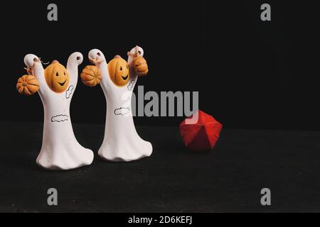 Zwei lustige essbare Zuckergeister mit Kürbissen auf schwarzem Hintergrund. Festliche Halloween-Leckereien. Stockfoto