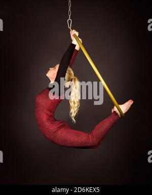 Eine schlanke blonde Frau-ein luftakrobatin in einem roten Anzug mit langen Haaren, führt Übungen in einem Luftring. Studioaufnahmen vor dunklem Hintergrund. Stockfoto