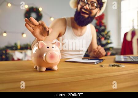 Glücklicher junger Mann beschließt, zu beginnen, sparen in der Neues Jahr und setzt Geld in Smiley Sparschwein Stockfoto