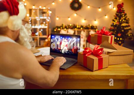 Vater Weihnachten sitzt am Schreibtisch mit Laptop und beobachtet Live-Show Mit Santa DJ auf lustige Nachtparty Stockfoto