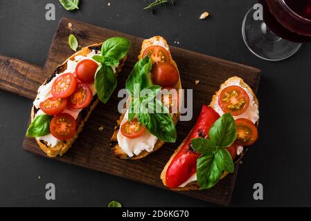 Bruschetta Sandwiches mit Tomaten, Frischkäse, gegrilltem Paprika und Basilikum auf Holzbrett, Nahaufnahme. Traditionelle italienische Snack für Wein - gegrillt b Stockfoto