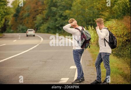 Wanderer auf der Straße. Reiseweg. Nur Freunde und weiter, spüren Sie die Freiheit. Reisen mit Freunden. Fahren Sie mit der Autostop. Hoffnungsloser Hexer. Männer versuchen, das Auto zu stoppen. Zwillinge gehen auf der Straße. Stockfoto