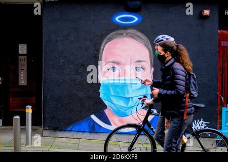 Junges Paar mit Fahrrad in einem schwarzen Gesicht Masken vorbei an dem Wandbild in der High Street, Manchester. Krankenschwester Debra Williams als Engel von AKSE. Neue Straße Stockfoto